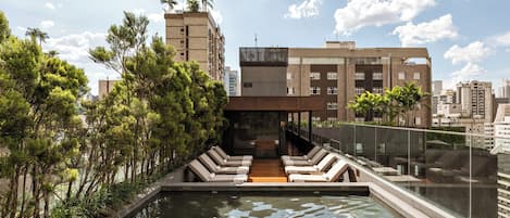 Un área de piscina en la azotea con sillas de descanso, una piscina pequeña y vistas de edificios circundantes.