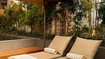 Un área de lounge en la azotea con dos tumbonas, un banco de madera y una pérgola.