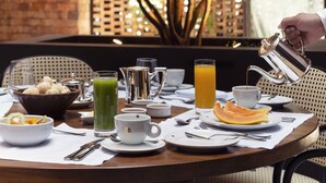 A breakfast table set with various dishes, including a bowl of fruit, a pitcher, a cup, and a glass of orange juice.