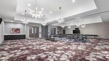A spacious conference room with a patterned carpet, modern chandeliers, and a large flat-screen TV.