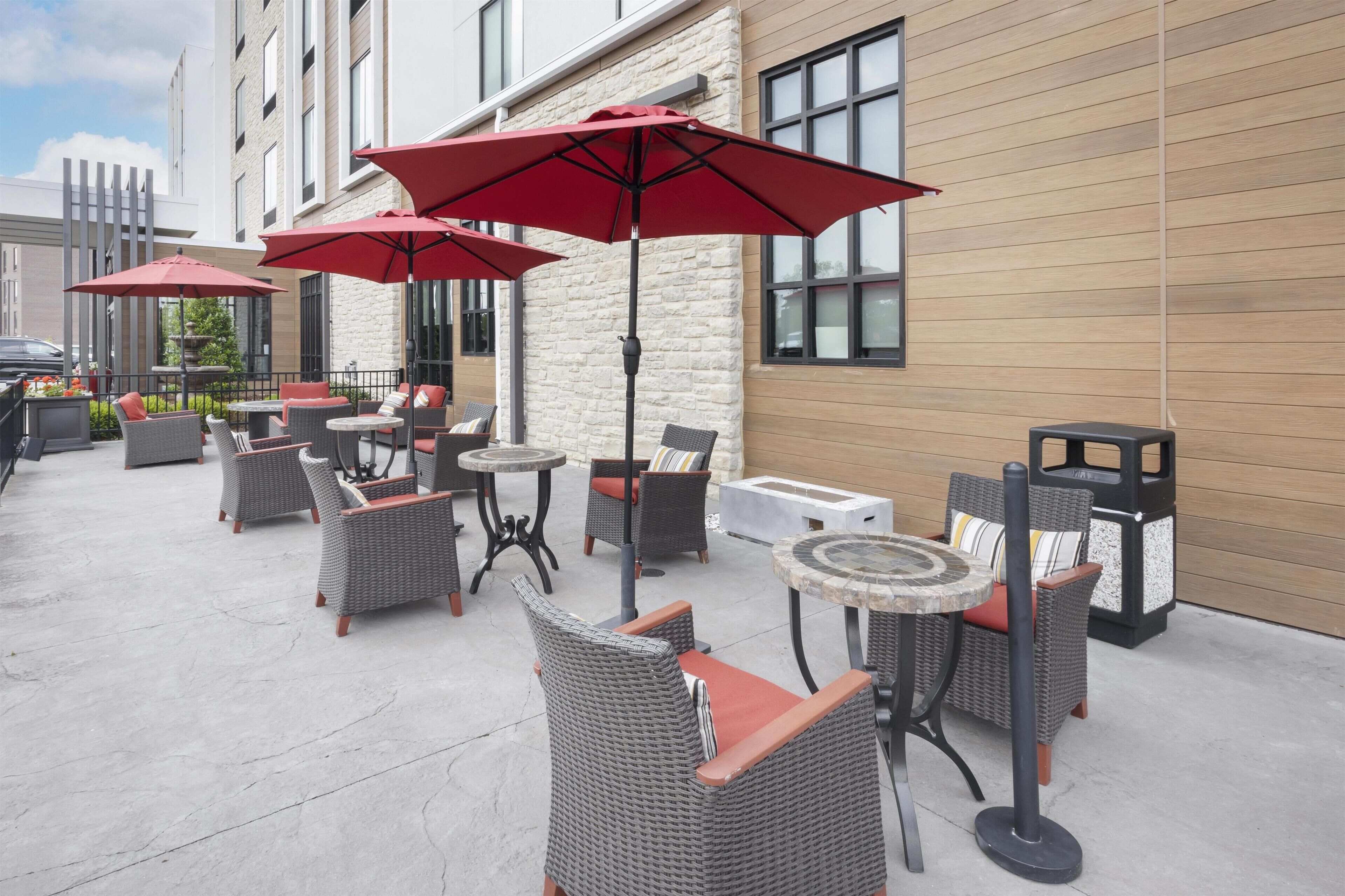 An outdoor patio with wicker furniture, red umbrellas, and a stone wall.