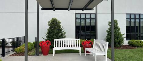 A covered outdoor seating area with two white benches and red flower planters.