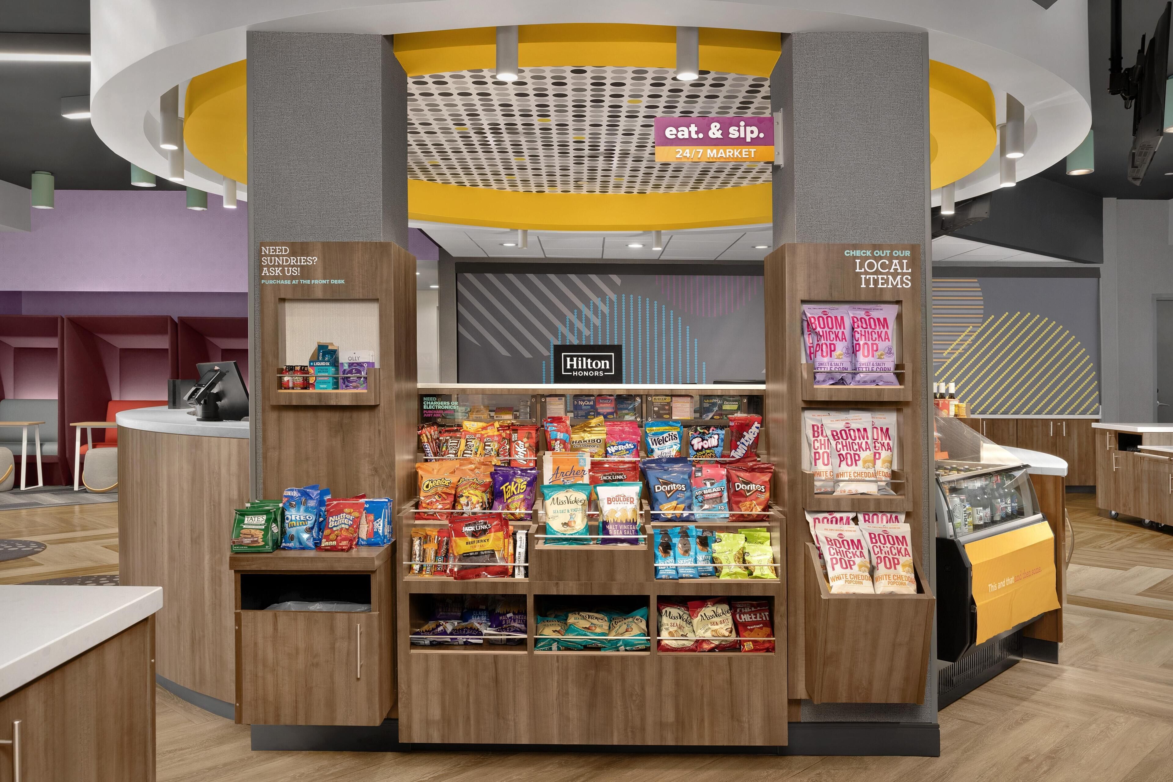 Een display met snacks van verschillende merken, een bord met '24/7 markt' en een Hilton Honors logo.