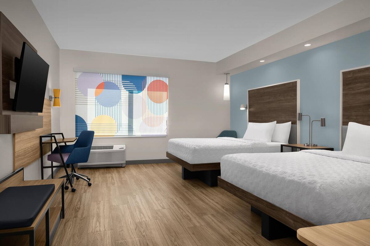 A modern hotel room with two beds, a desk, a chair, and a TV.