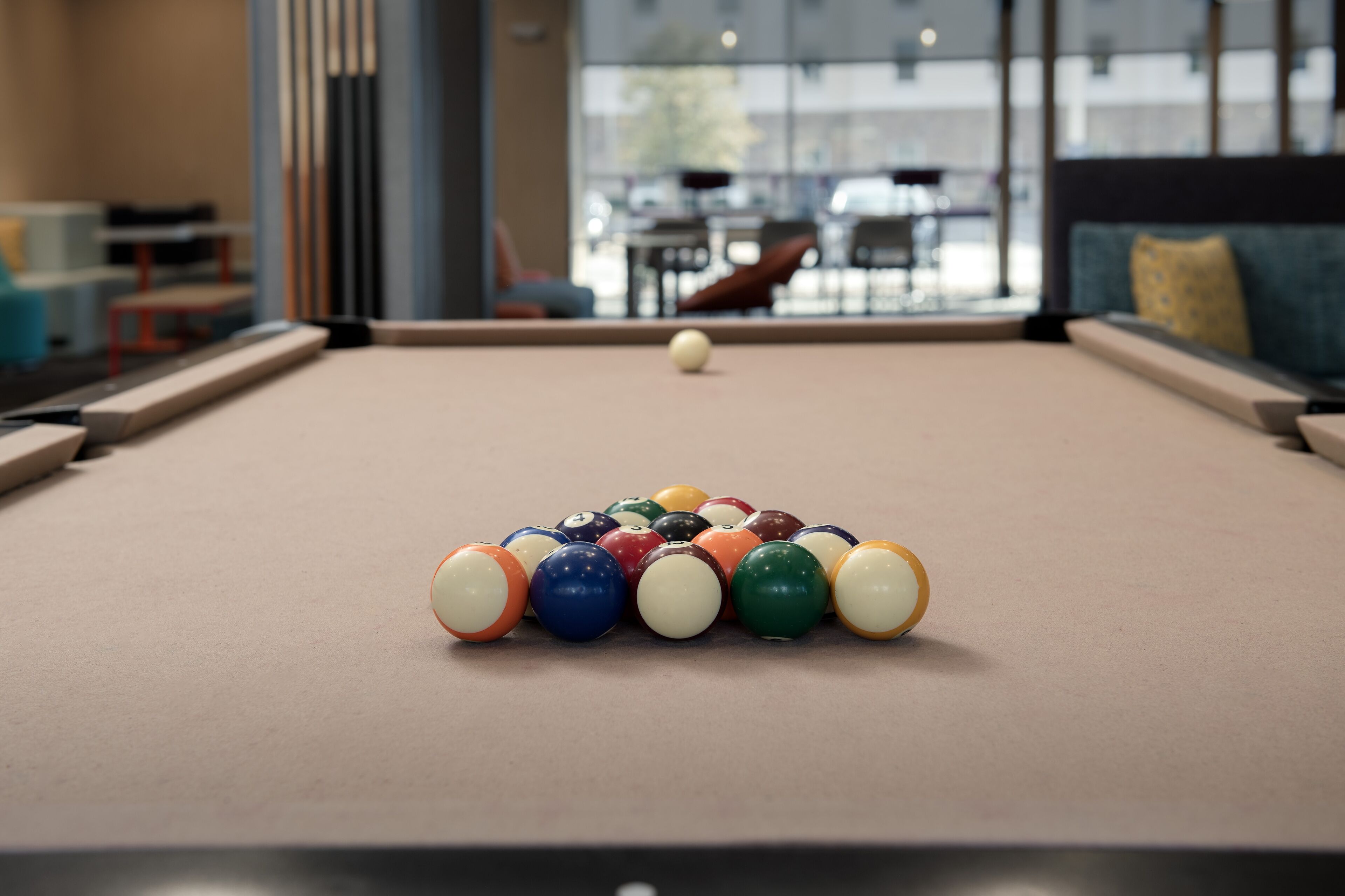 Une table de billard avec un jeu de billes au centre, un canapé et une fenêtre en arrière-plan.