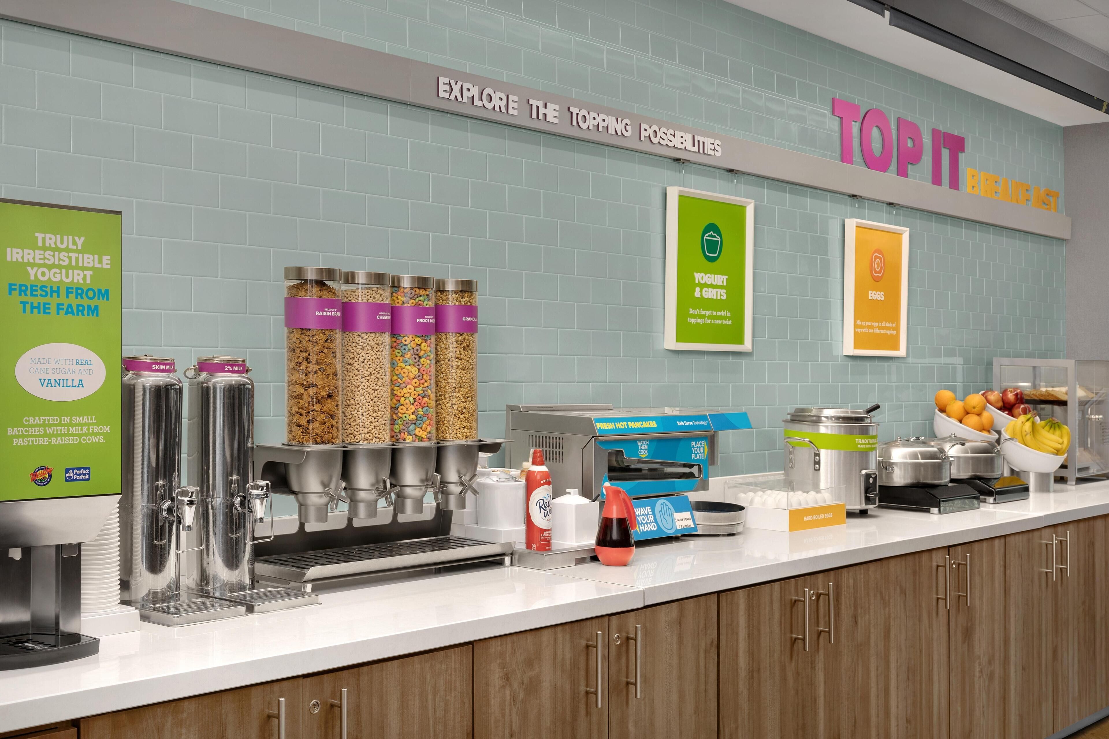 A breakfast bar with yogurt dispensers, a coffee machine, and a sign reading 'TOPIT BREAKFAST'.