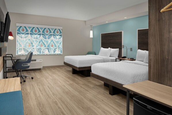 Une chambre d’hôtel avec deux lits, un bureau, une chaise, une télévision et une fenêtre ornée d’un motif décoratif.