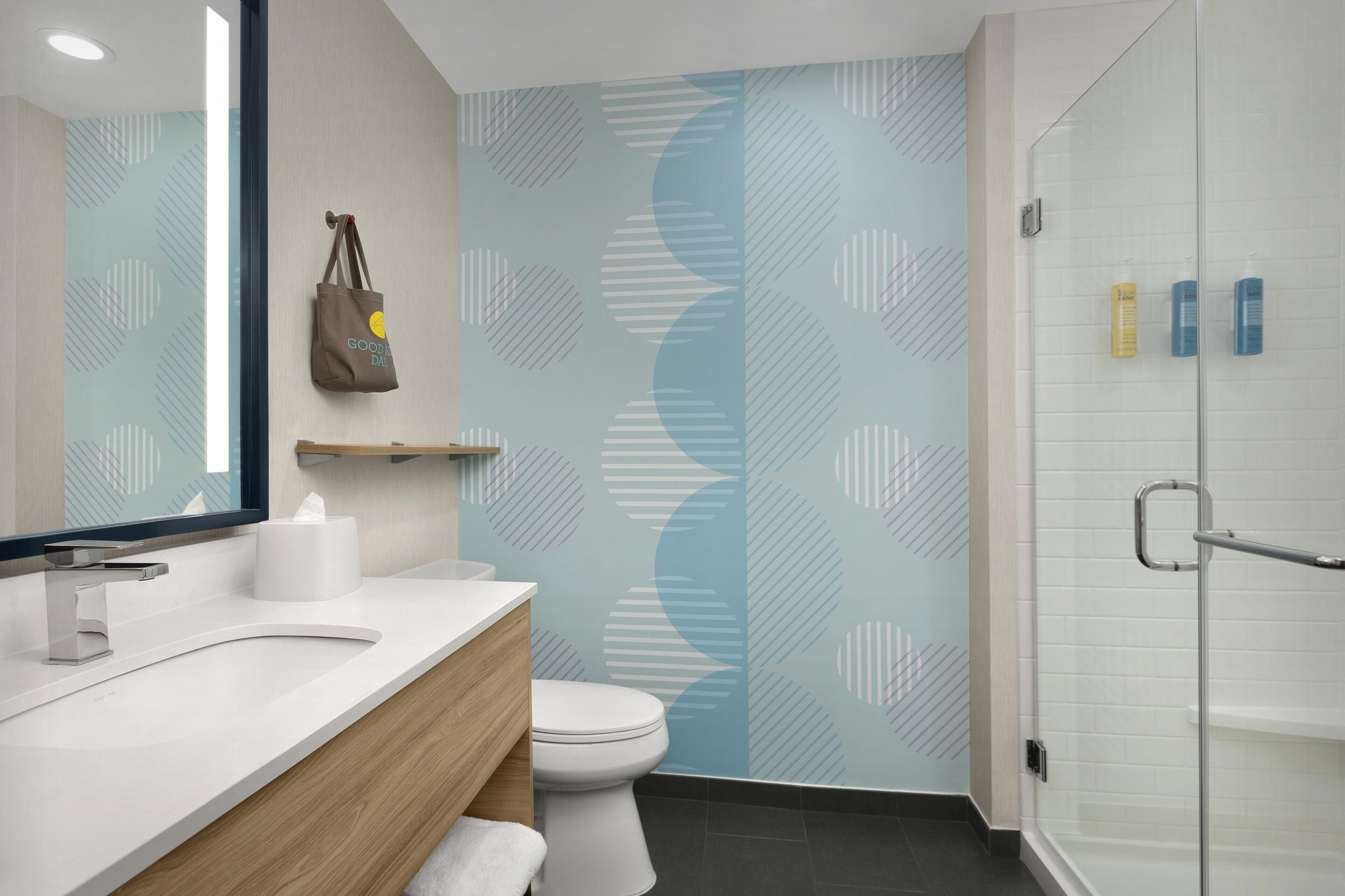 A modern bathroom with a white sink, wooden vanity, a toilet, and a glass shower enclosure.