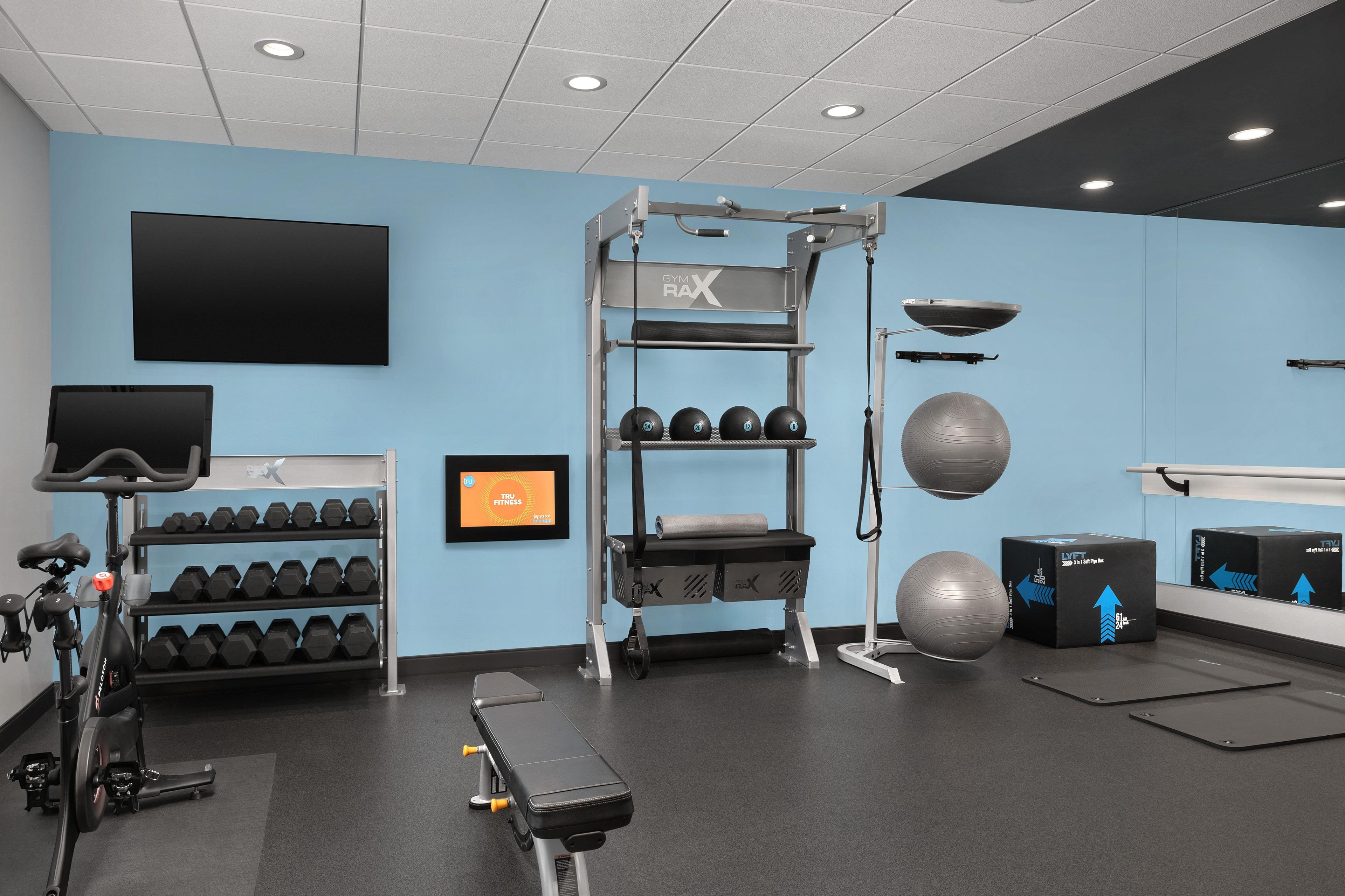 A gym with exercise equipment, dumbbells, a bench, and a wall-mounted TV.