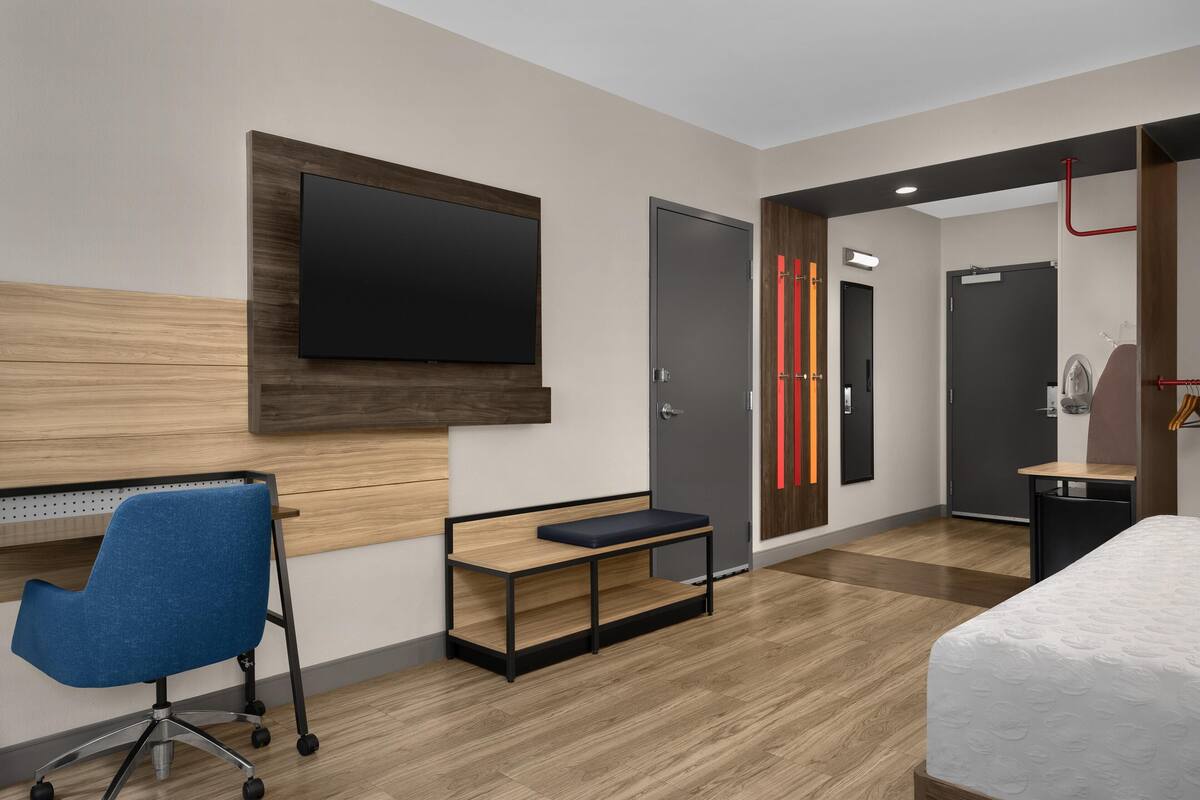 A modern hotel room with a flat-screen TV, a desk with a chair, a bed, and a shower area.