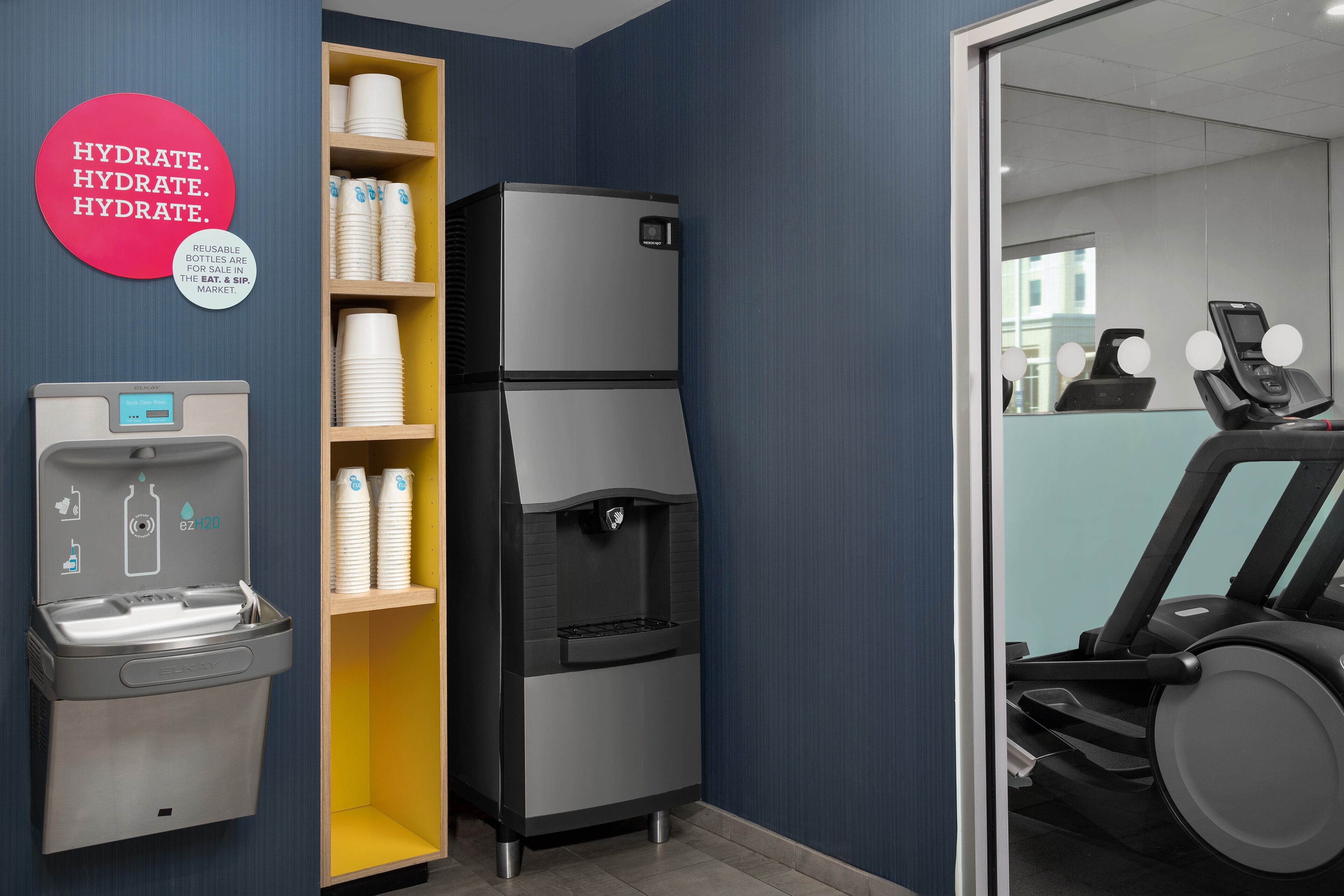 A room with a water dispenser, a refrigerator, and a treadmill.