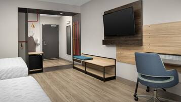 Habitación de hotel con dos camas, un escritorio con silla, un televisor montado en la pared y zona de ducha.