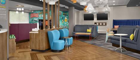 Eine moderne Hotelhalle mit einer Rezeption, blauen Sesseln, einem grauen Sofa und einem an der Wand befestigten Fernseher.