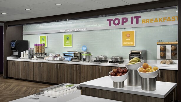 A breakfast area with a counter displaying various food items and a sign reading "TOP IT BREAKFASTS". - Tru by Hilton Fayetteville I-95, NC (Fayetteville)