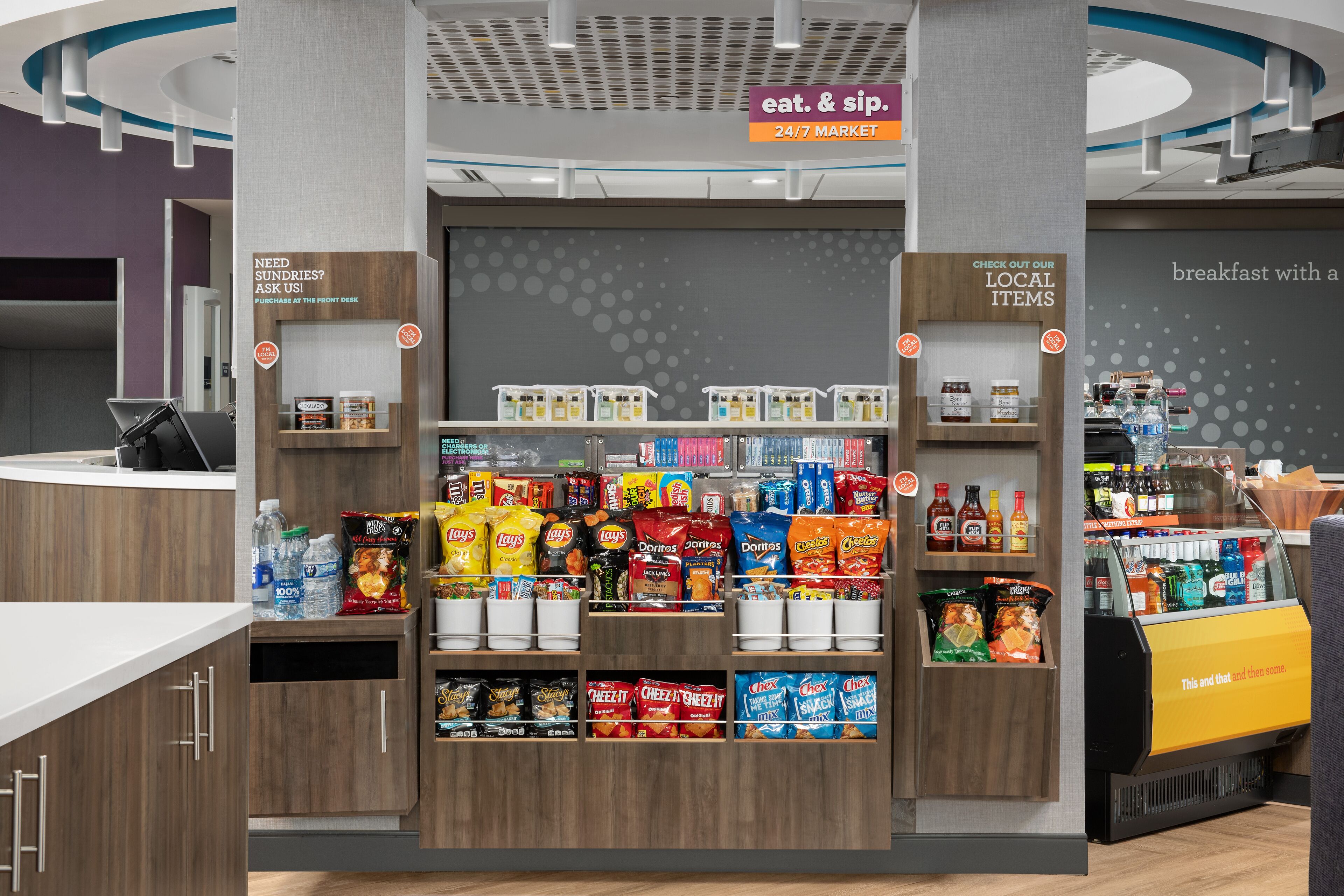 A snack kiosk with a variety of chips and snacks, a front desk area, and a sign indicating a 24/7 market.