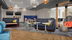 A modern lounge area with sofas, tables, and hanging chairs, featuring a herringbone floor pattern and contemporary lighting fixtures. - Tru by Hilton Fayetteville I-95, NC (Fayetteville)