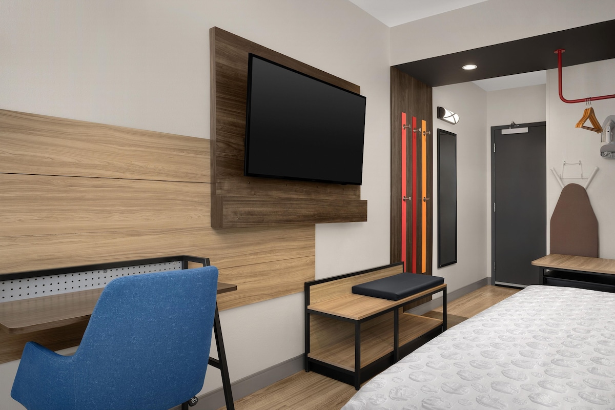 A hotel room with a bed, a TV mounted on the wall, a desk, and a chair.