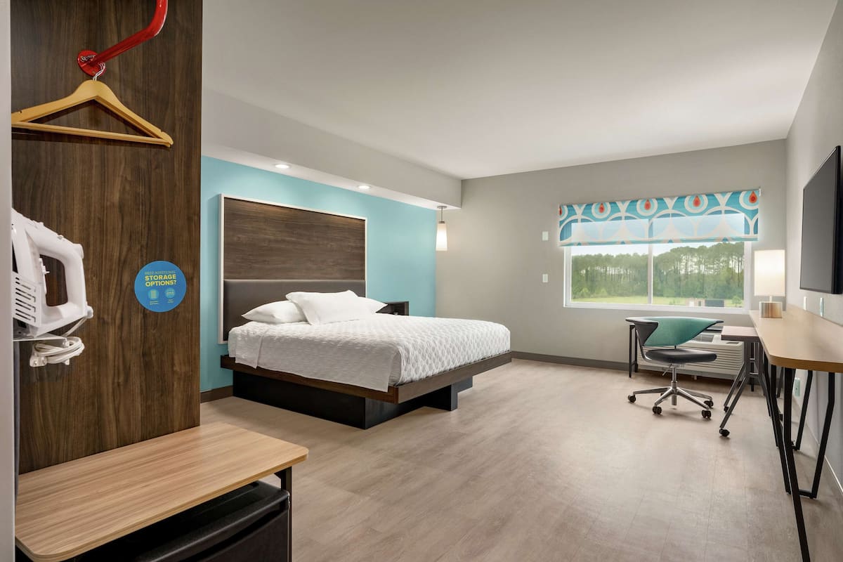 Una moderna camera d'albergo con un letto, una scrivania, una sedia e un'ampia finestra.