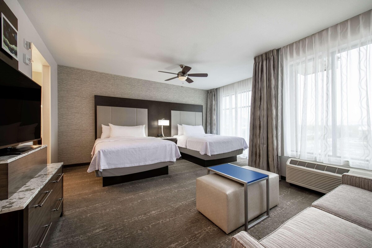 Une chambre d’hôtel avec deux lits, une télévision, un bureau et un ventilateur de plafond.