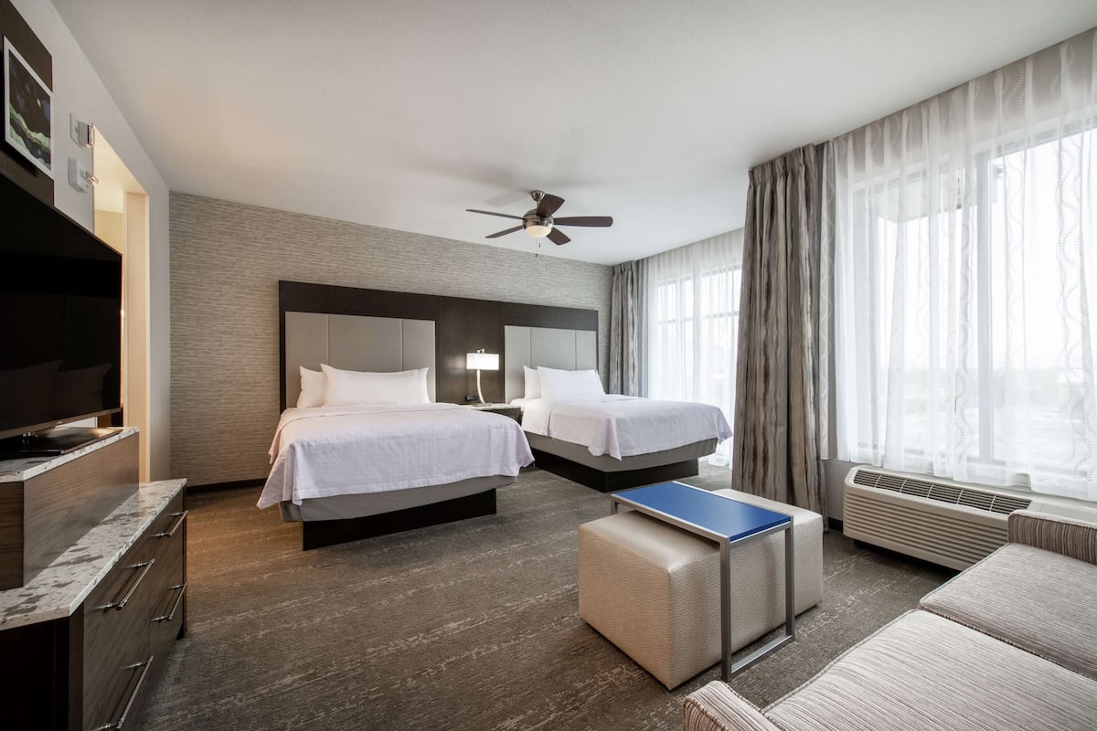 Hotellihuone, jossa on kaksi sänkyä, taulutelevisio, työpöytä ja kattotuuletin.