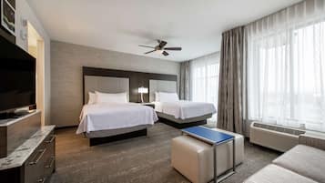 A hotel room with two beds, a flat-screen TV, a desk, and a ceiling fan.