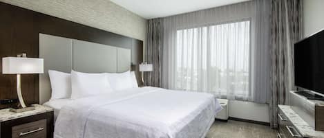 Una habitación de hotel con una cama grande, un ventilador de techo, un televisor y un ventanal con cortinas.
