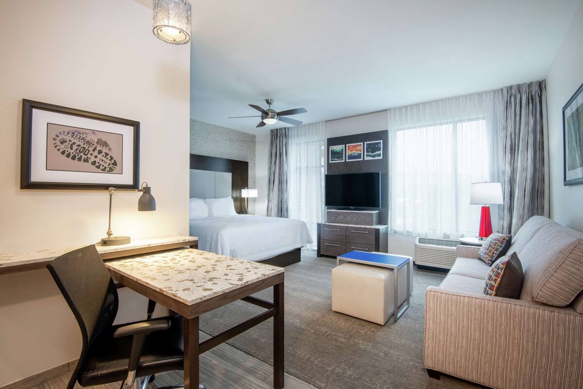 Hotellihuone, jossa on sänky, sohva, televisio, työpöytä ja tuoli.
