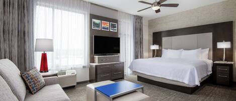 A modern hotel room with a large bed, a flat-screen TV, a sofa, a coffee table, and a ceiling fan.