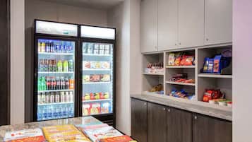 A hotel room with a minibar, a refrigerator stocked with beverages, snacks, and a table with books.