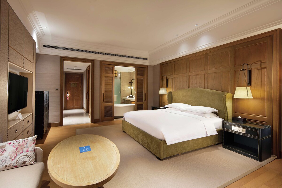 A hotel room with a bed, bedside table, lamp, TV, and a round table.