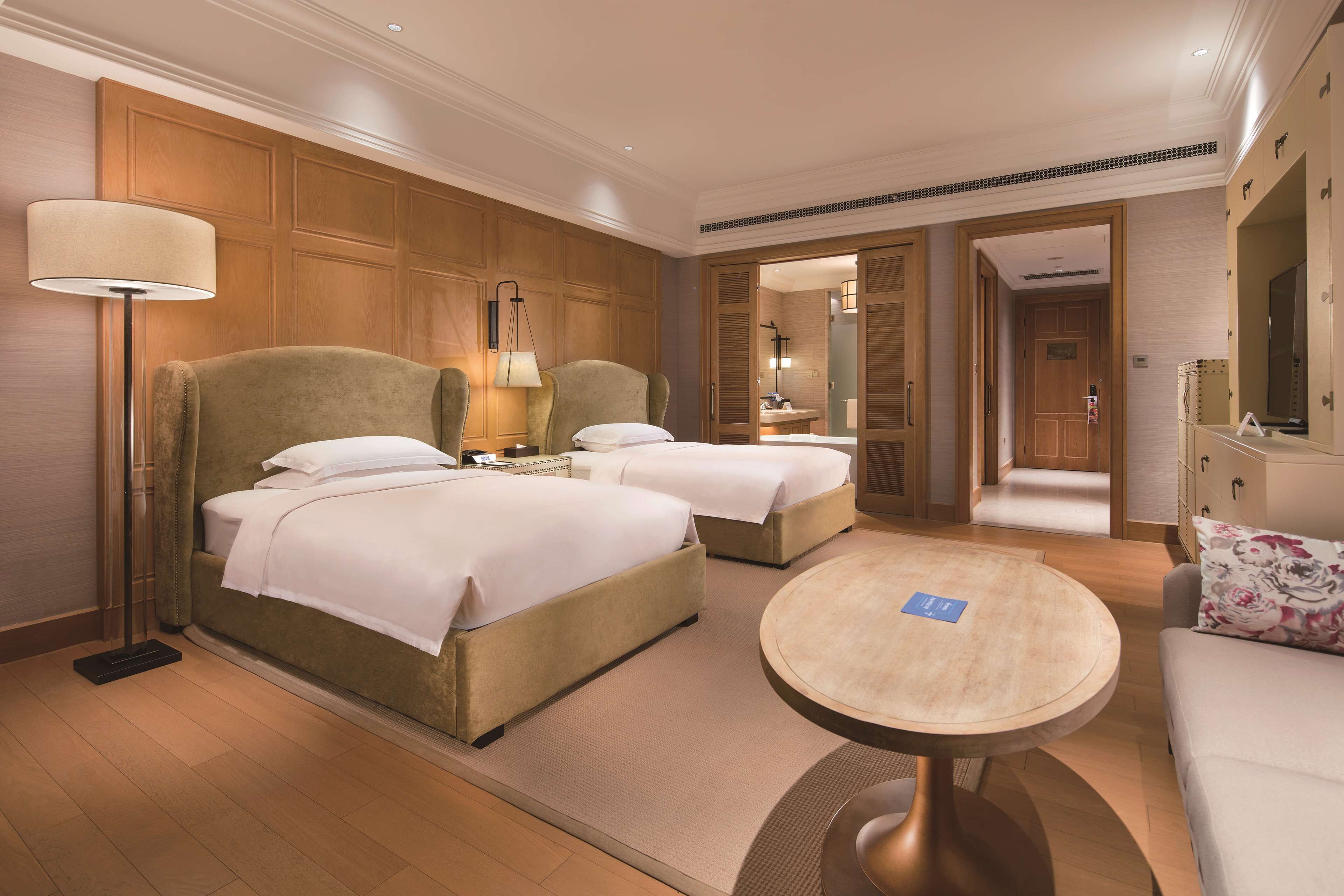Habitación de hotel con dos camas, una mesa de centro redonda, un sofá y un espejo grande.