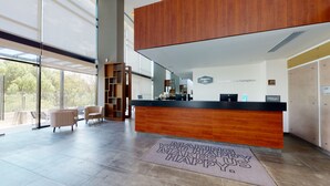 Un moderno hall de hotel con un mostrador de recepción de madera, un área de descanso con sillas estampadas y un ventanal con vistas al exterior.