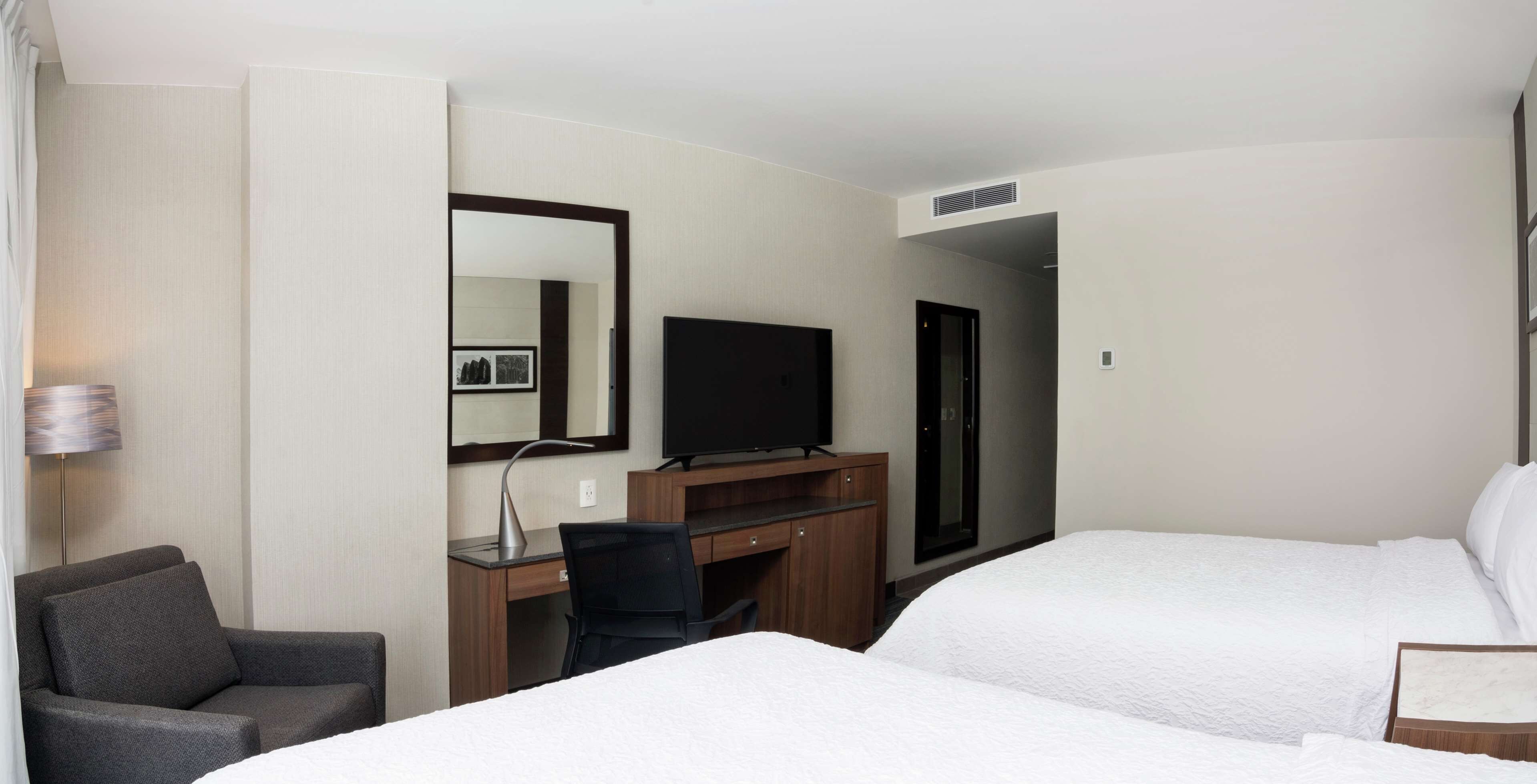 A hotel room with a bed, a desk with a chair, a television, and a mirror.