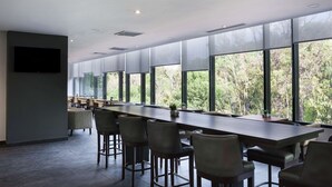 Una sala de conferencias moderna con una mesa larga, múltiples sillas y ventanas grandes que dan a vistas de árboles.