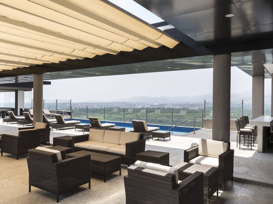 A rooftop lounge with wicker furniture, a pool, and a view of the cityscape.