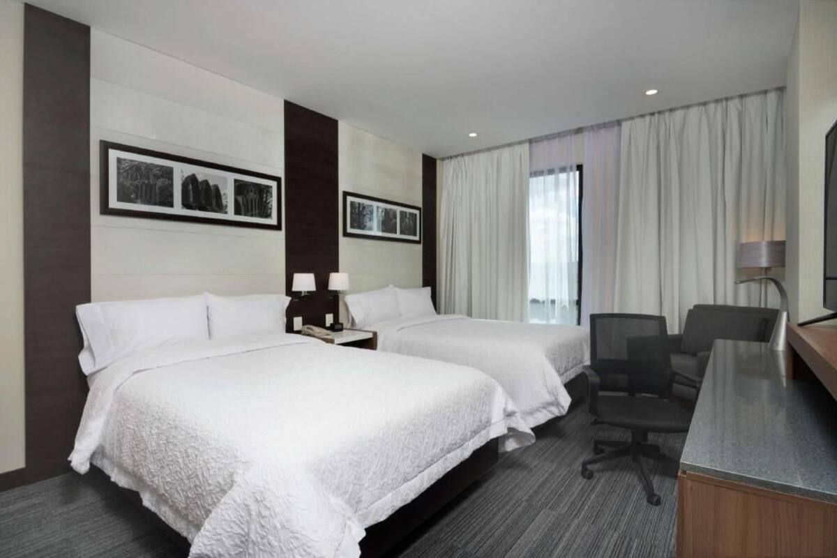 A hotel room with two beds, a desk, a chair, and a TV.