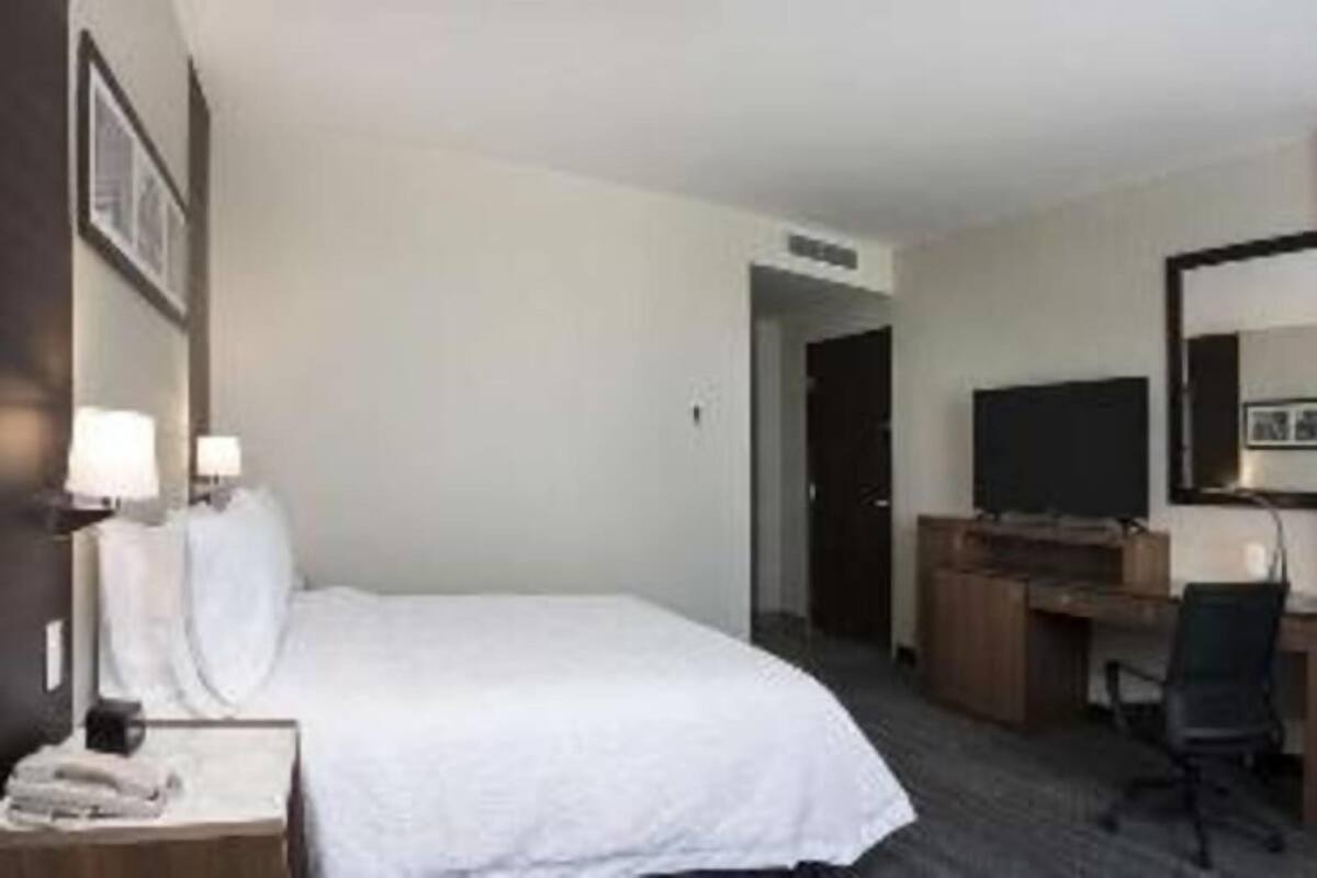 A hotel room with a bed, a desk, a chair, a TV, and a mirror.