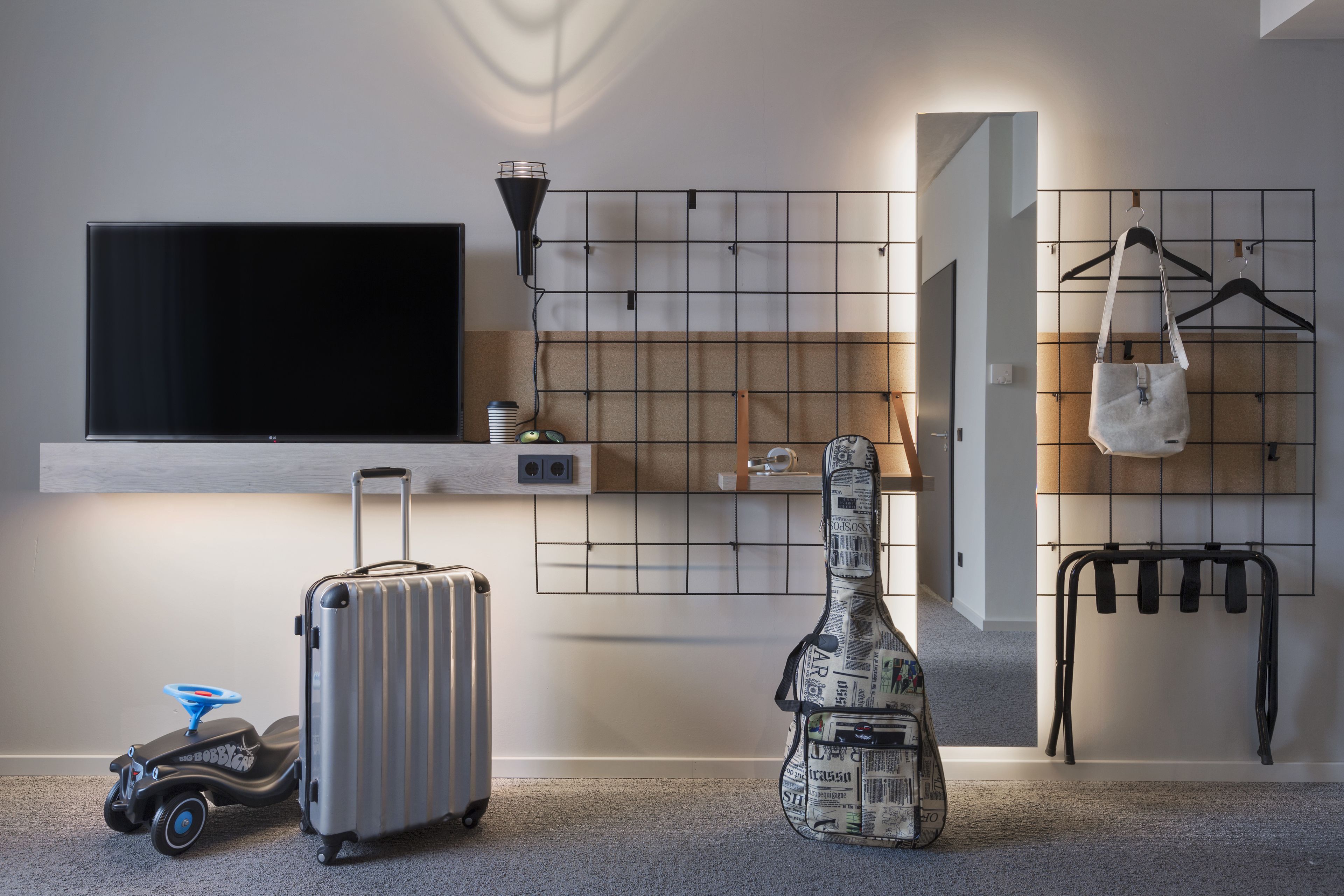 A room with a flat-screen TV, a guitar, a suitcase, and a toy car.