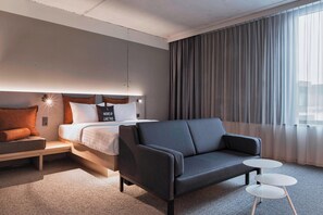 Een moderne hotelkamer met een bed, een bank, een klein tafeltje en een groot raam met gordijnen.