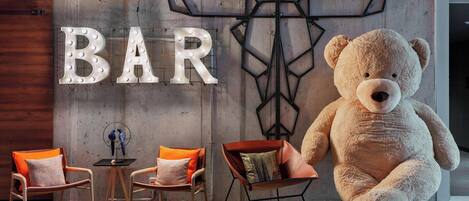 A bar area with a large teddy bear, two chairs, and a 'BAR' sign.