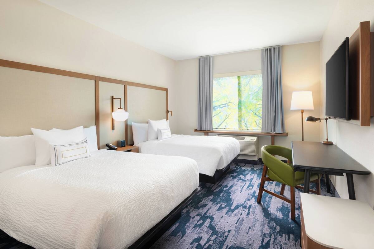 A hotel room with two beds, a desk, a chair, a TV, and a window with curtains.