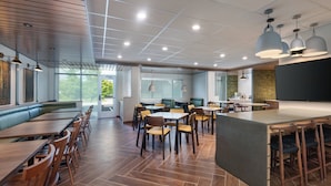 A modern restaurant with wooden flooring, multiple seating areas including booths and tables, pendant lighting, and large windows offering views of the outdoors. - Fairfield Inn & Suites by Marriott Lexington East/I-75 (Lexington)