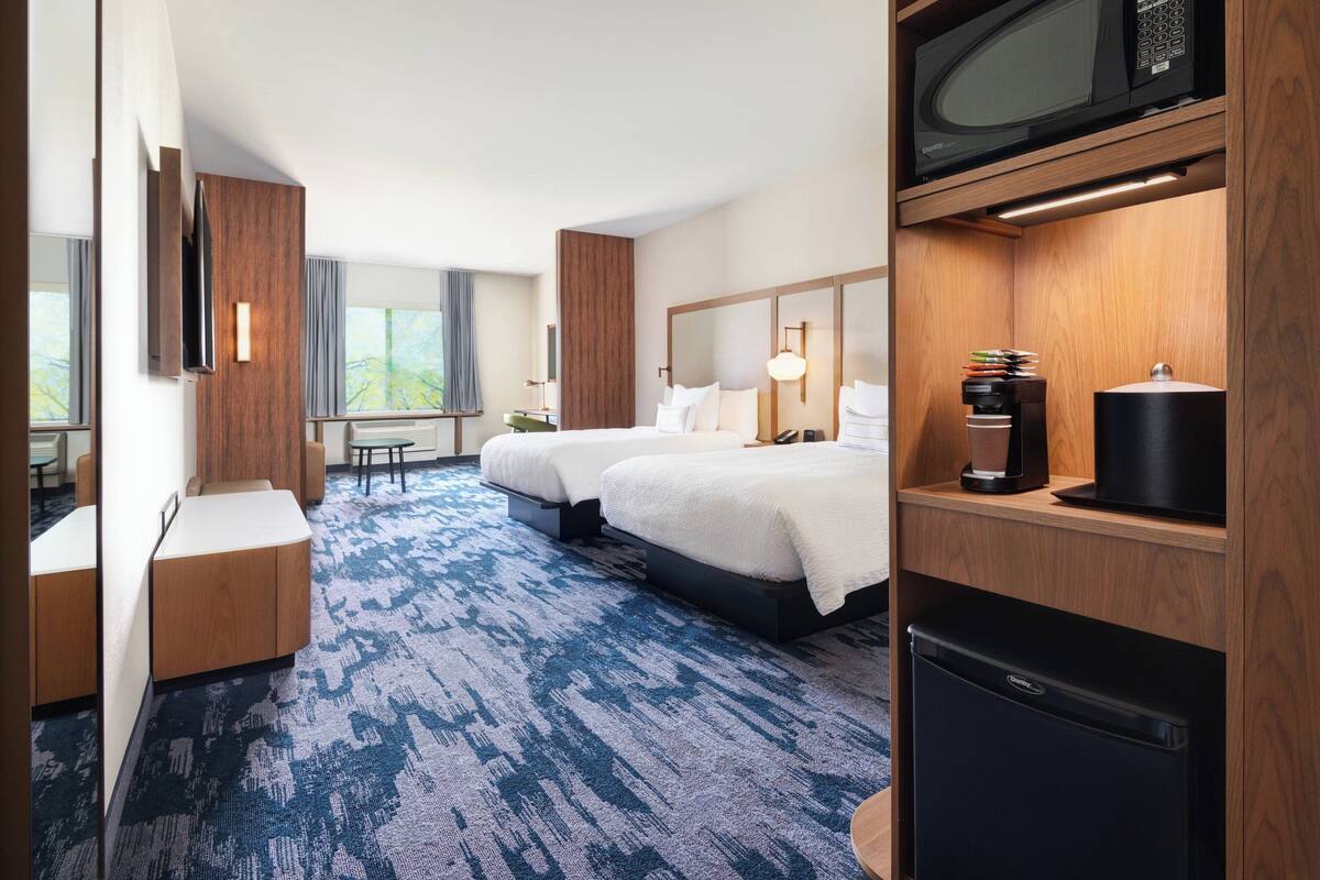 A hotel room with two beds, a desk, a microwave, a coffee maker, and a refrigerator.