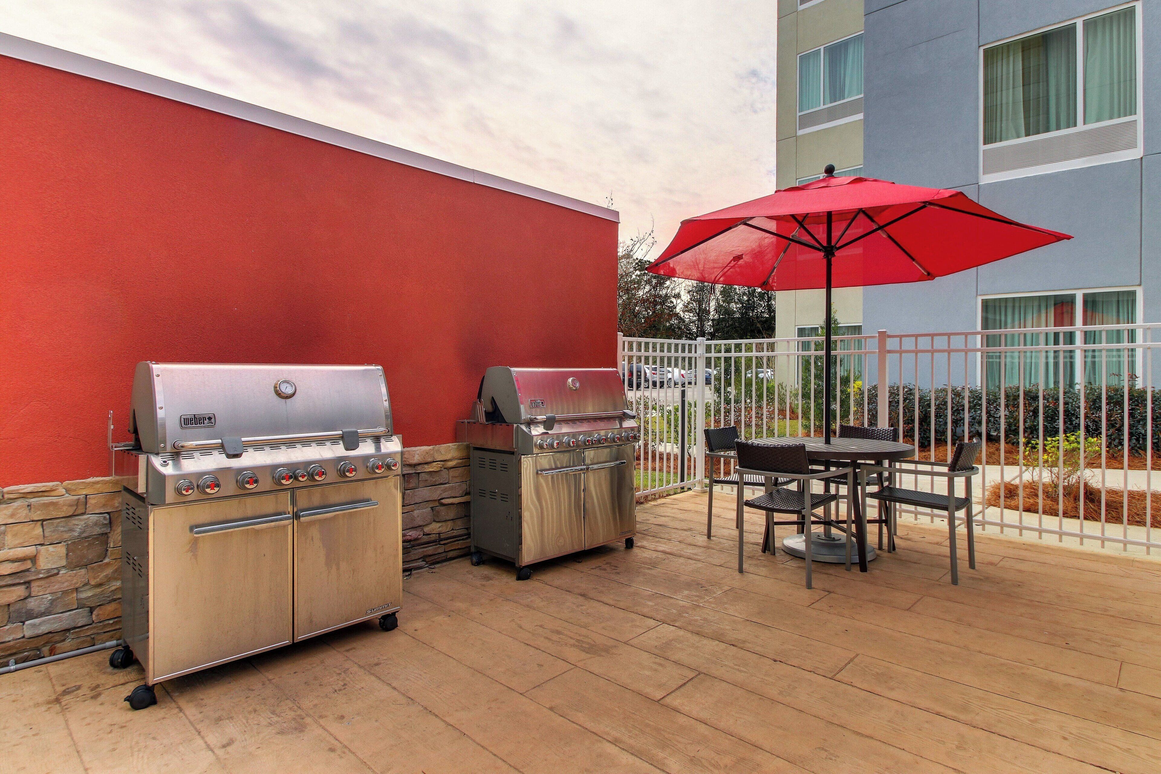 An outdoor patio with two Weber grills, a red umbrella, and a table with chairs.