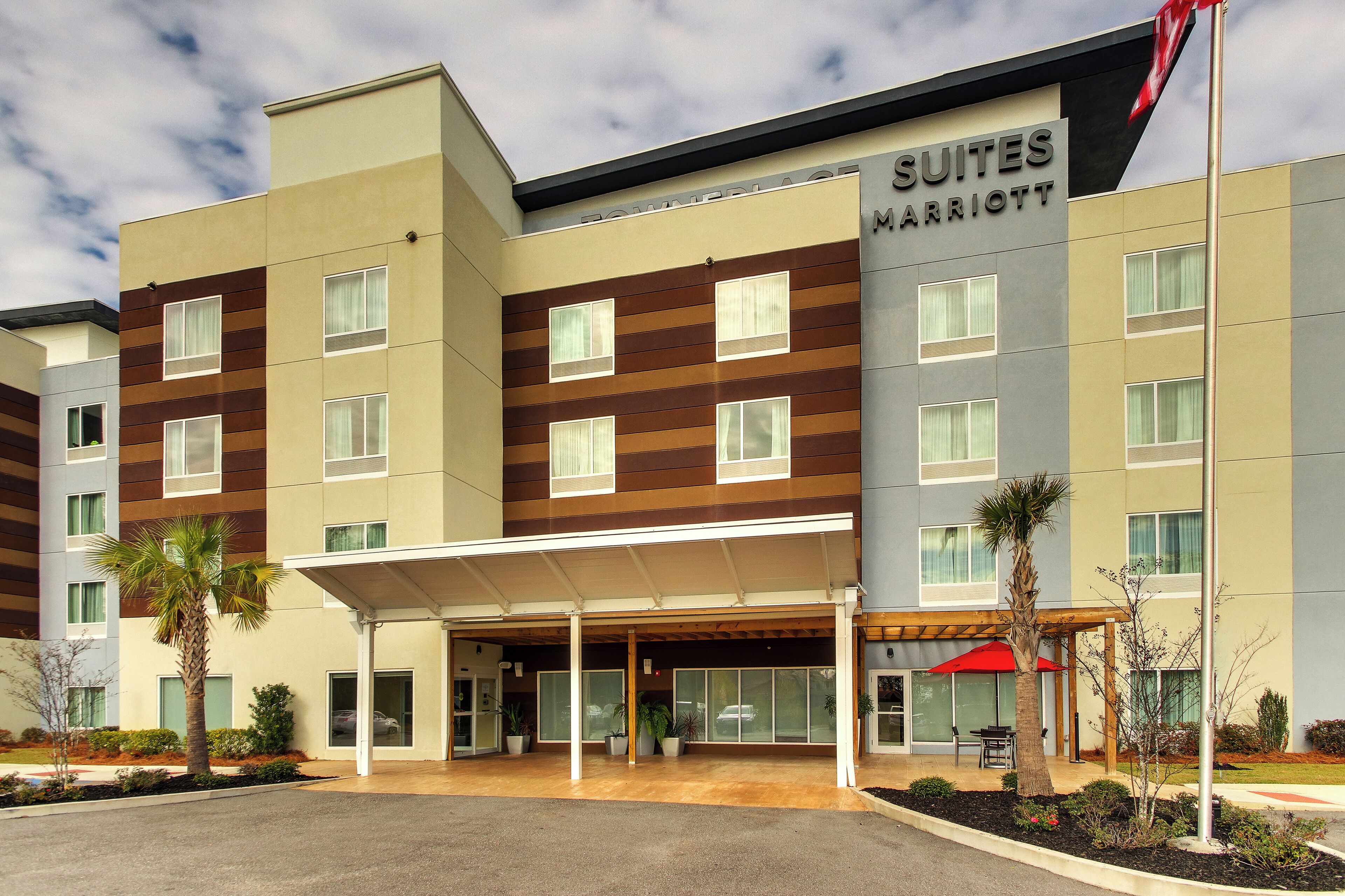 Un hôtel moderne doté d’une entrée couverte, de plusieurs étages et d’une enseigne indiquant qu’il s’agit d’un hôtel Marriott Suites.