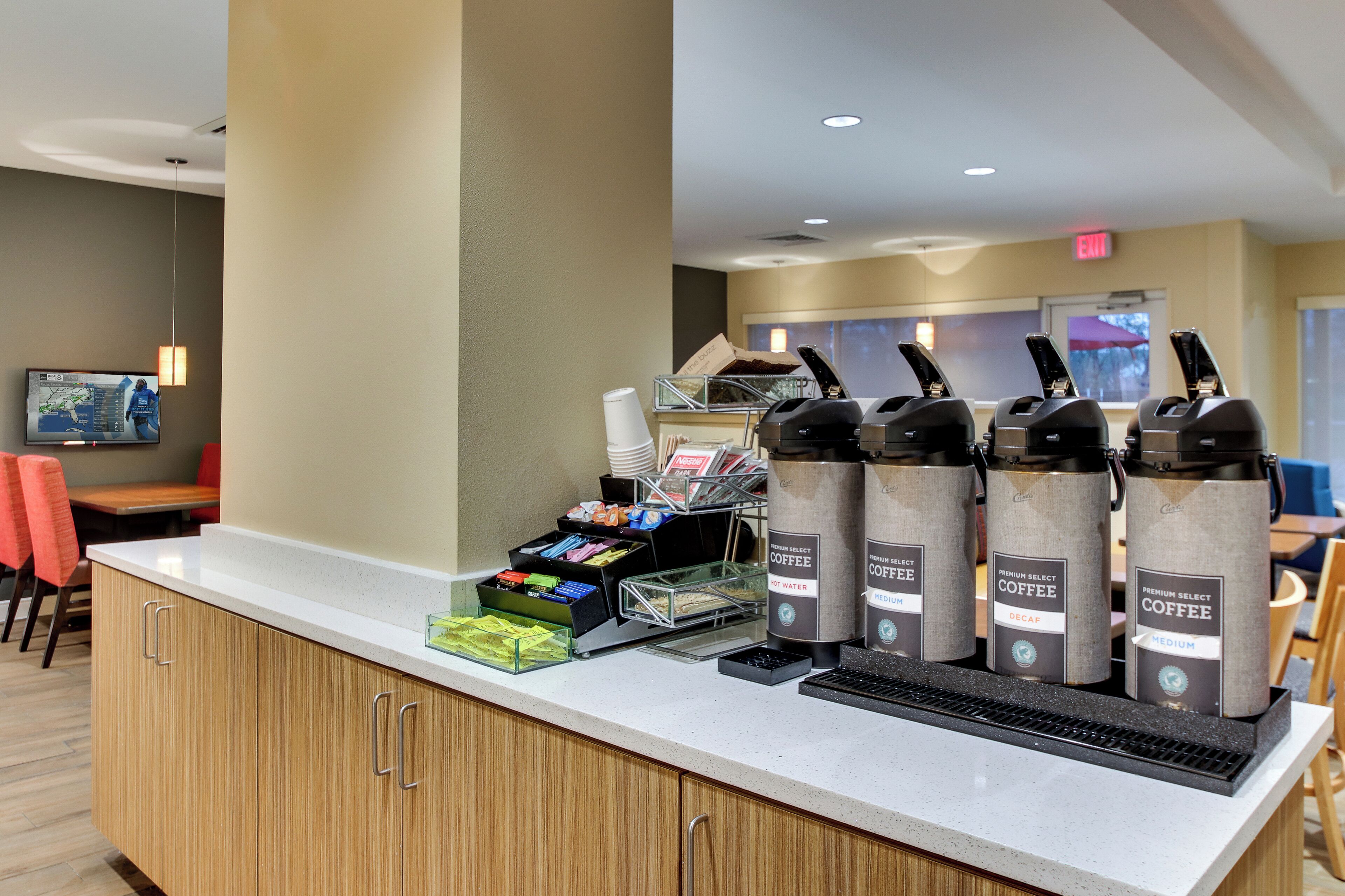 Una estación de café con varios dispensadores de café, un dispensador de bebidas y una variedad de cápsulas de café y snacks.