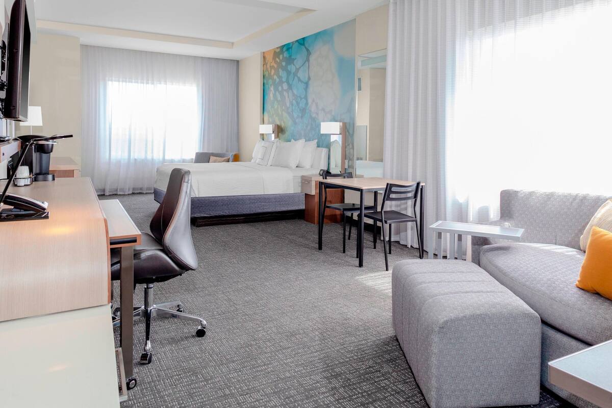 A hotel room with a bed, desk, chair, sofa, and a large window with curtains.