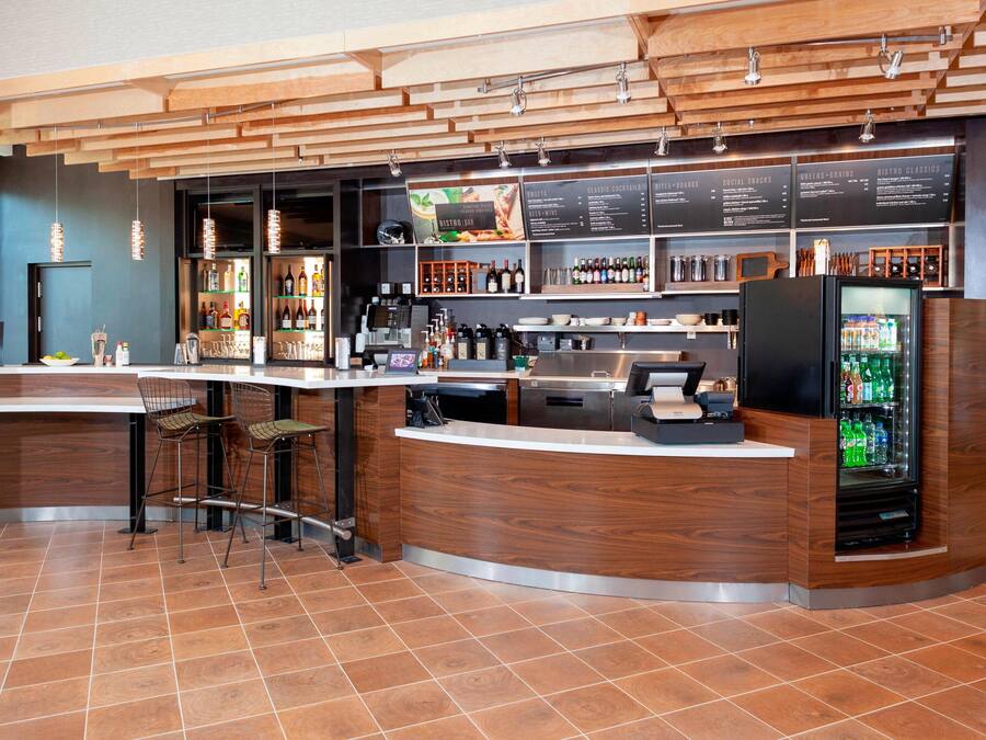 A modern bar area with a wooden counter, bar stools, and a refrigerated display.
