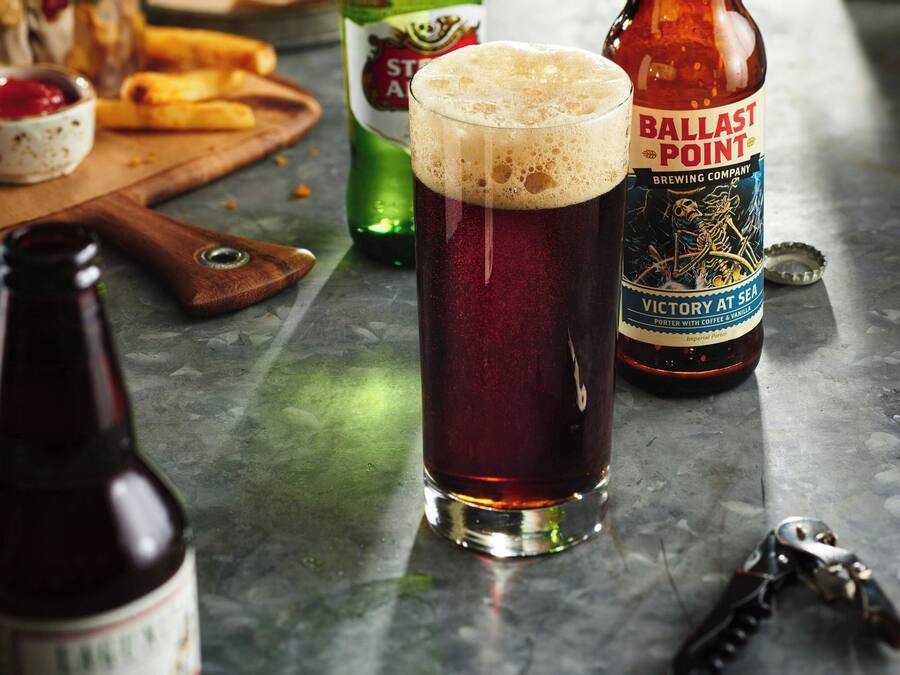 A glass of beer, a bottle of Ballast Point beer, and a bottle of Liguus beer on a table.