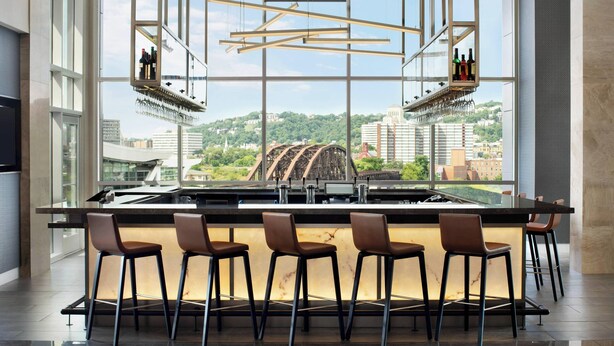 A modern bar area with a large window overlooking a bridge and cityscape. - AC Hotel Pittsburgh Downtown (Pittsburgh)